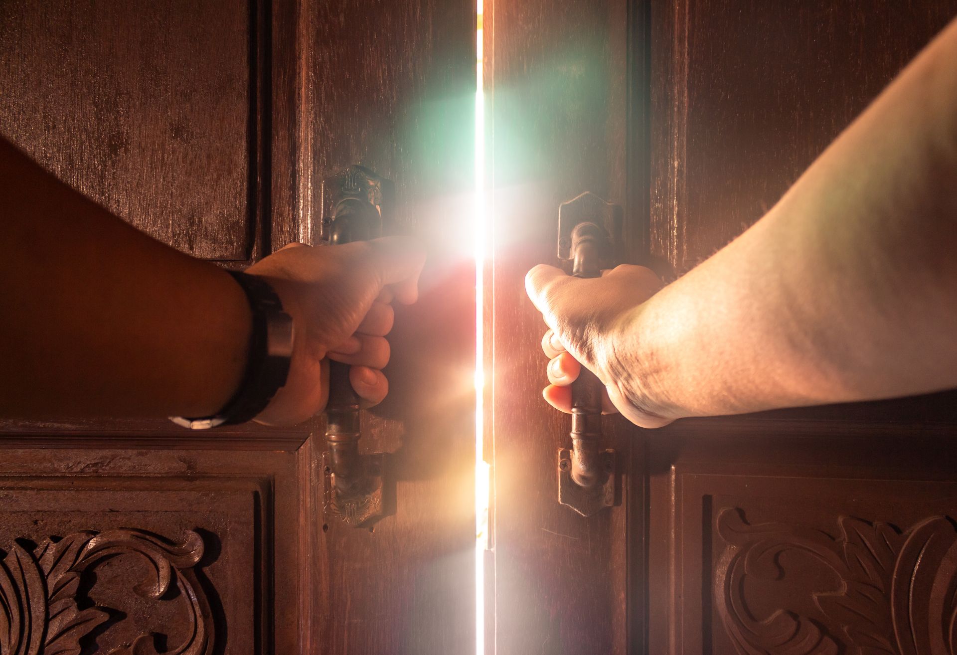 Image of hands opening a door behind which is a strong light